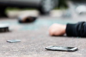 A broken phone lying next to an unconscious person on the pavement