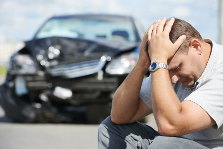 a man kneels and holds his head following a car accident. 