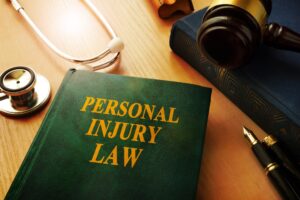 A green book titled 'personal injury law' with a gavel, a pen, and a blue book next to it on an oak table.