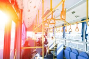Inside of a fairly empty bus with the sun shining through the bus windows on the left. 