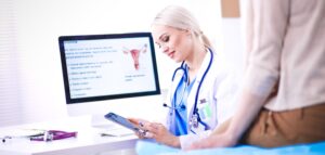 a gynaecologist in front of a computer looking at test results on a phone and explaining to a patient.