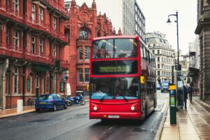 A red double decker bus driving down a street in the rain