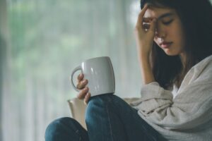 Woman sat down and holding a cup with one hand and her head with her other hand