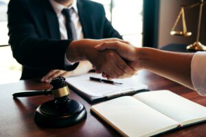 A solicitor in a black suit and tie, shaking hands with their client across a table after discussing compensation payouts.