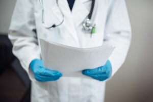 A doctor in a white coat with blue gloves holding patient records