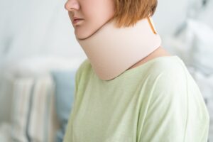 A close-up of a person with red hair a a light green top, wearing a large neck brace.