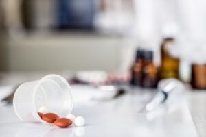 A clear cup overturned on a table with red and white pills spilling out