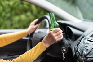 A woman driving with a bottle of beer in her hand. 