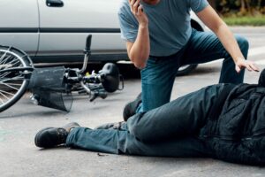 A driver calling an ambulance while kneeling over an injured cyclist.