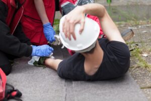 A construction worker in a white hard hat lays injured on the ground