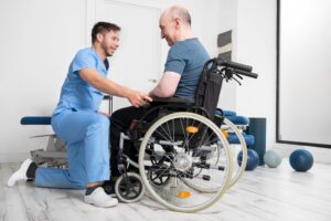 A healthcare assistant kneels to talk to a patient in a wheelchair.