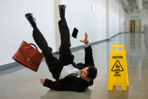 A business man slipping next to a wet floor sign at work