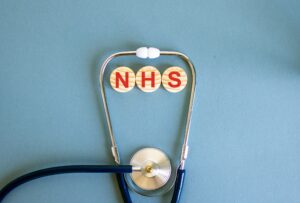 The letters 'NHS' in red on 3 separate circular wooden blocks in the middle of a stethoscope.
