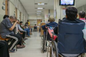 A crowded NHS hospital waiting room with people sat in every seat. 