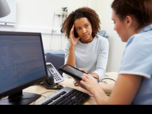 A patient holds their head in one hand while talking to a nurse.