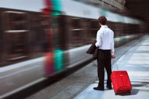 A person standing on a platform and holding a red carry case while a train passes.