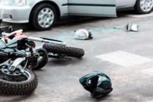 Helmet and crashed motorbike laying on the ground next to a damaged car