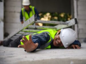 injured construction worker lying on floor with ladder fallen on top of him