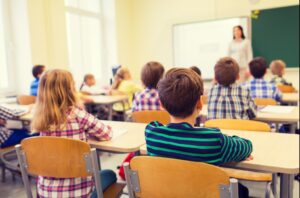 Children sitting in a classroom facing the teacher at the front.