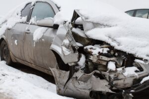 A car has seriously crashed on a winter road and the front of it is seriously damaged.