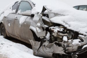 A heavily damaged grey car is covered in snow.