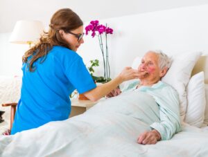 A medic in blue scrubs attends to an elderly man in a hospital bed.