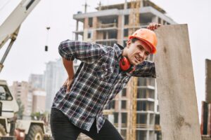A construction worker bent over holding their back in pain