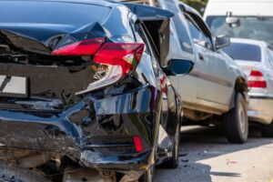 A black car rear-ended a silver car. Both car have damage. 
