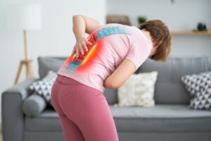 A woman bent over holding her back in pain.