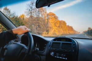 A driver holding onto a steering wheel on a clear autumn day. 