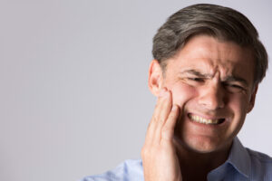 Man holds his right cheek and has a pained expression on his face.