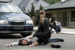 A woman kneels over a man at the scene of a road traffic accident.