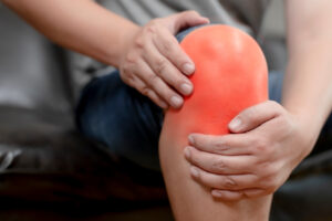 Someone holding their knee in pain which is highlighted in red.