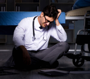 An upset doctor sat on the floor in front of gurney. 
