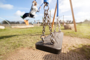 A close-up shot of a swing in a park, with children on more swings in the background.